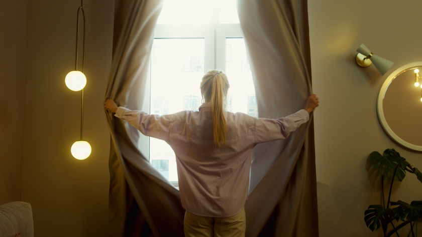 A woman opening a white curtain.